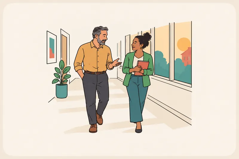 A manager and an employee walk down a sunny hallway together; the manager explains one point while the employee listens and holds a notebook.